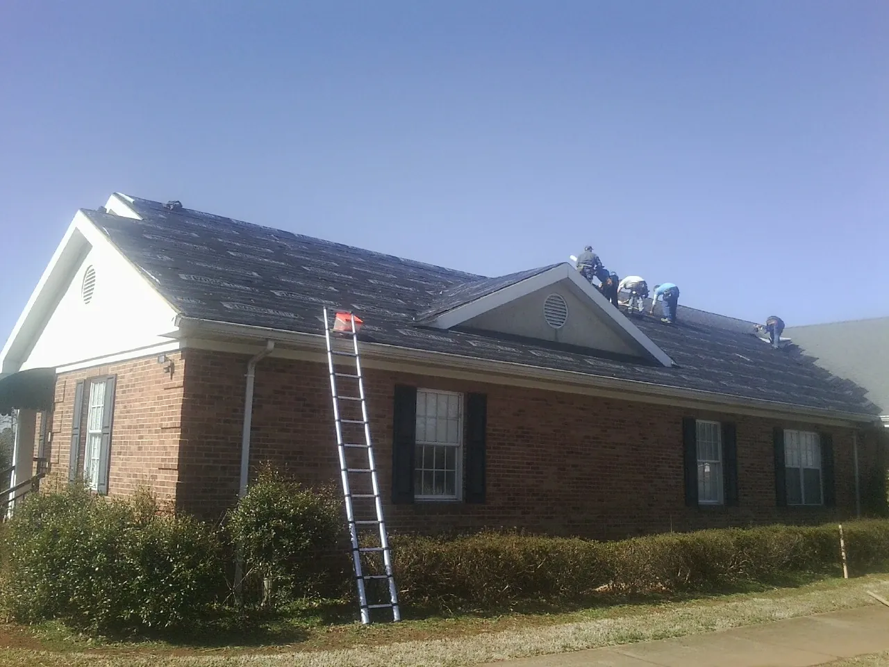 Crew tearing shingles off a brick ranch roof with a ladder set — Metal Roof Repair work by our crew in Greenbank