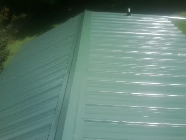 New green metal panels meeting at the ridge of a roof — Flat Roof Repair work by our crew in Greenbank