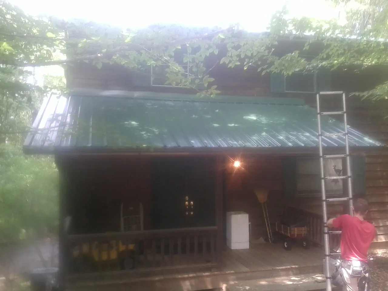 Worker on a ladder at the green porch roof of a wooded cabin in Greenbank