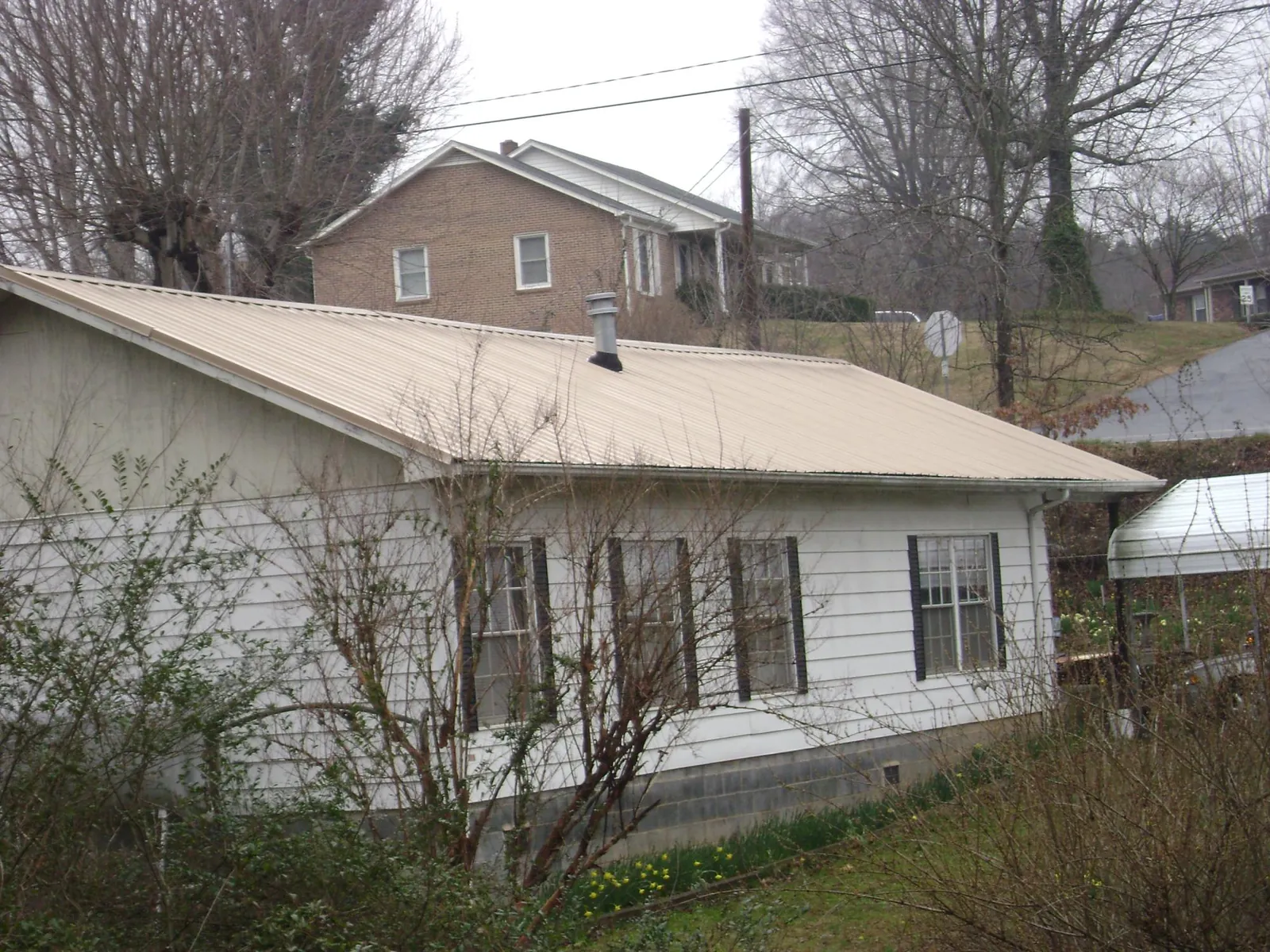 Tan metal roof on a white sided house set into a hillside — Commercial Roofing by Roofing Brothers in Greenbank